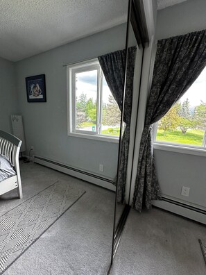 A room with a bed, a chair, a window with curtains, and a picture on the wall.
