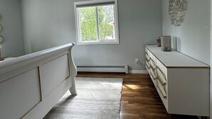 A room with a white dresser, a white radiator, a window with a view of trees, and a ceiling light. - 3 Bedroom-Queen Beds-UMed-Stunning Mountain Views-Trails to lakes (Anchorage)