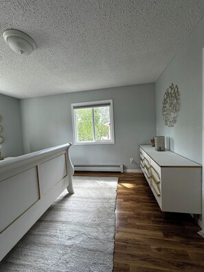 Ein Zimmer mit weißem Schminktisch, einer weißen Heizung, einem Fenster mit Blick auf Bäume und einer Deckenleuchte.