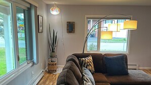 A modern living room with a sectional sofa, a floor lamp, and a large window providing a view of the outdoors. - 3 Bedroom-Queen Beds-UMed-Stunning Mountain Views-Trails to lakes (Anchorage)