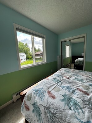A bedroom with a bed, a window, and a door leading to another room.