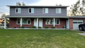A two-story residential building with a covered porch, a garage, and a well-maintained lawn. - 3 Bedroom-Queen Beds-UMed-Stunning Mountain Views-Trails to lakes (Anchorage)