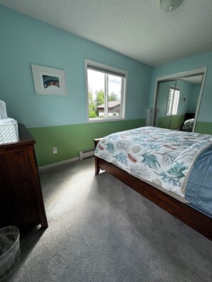Ein Schlafzimmer mit Bett, Kommode, Fenster und Spiegel.