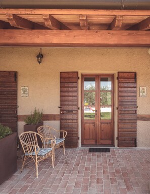 A covered patio with two wooden doors, wicker chairs, and a brick floor. - FARMHOUSE QUERCETO - APARTMENT SUNFLOWER (Gubbio)