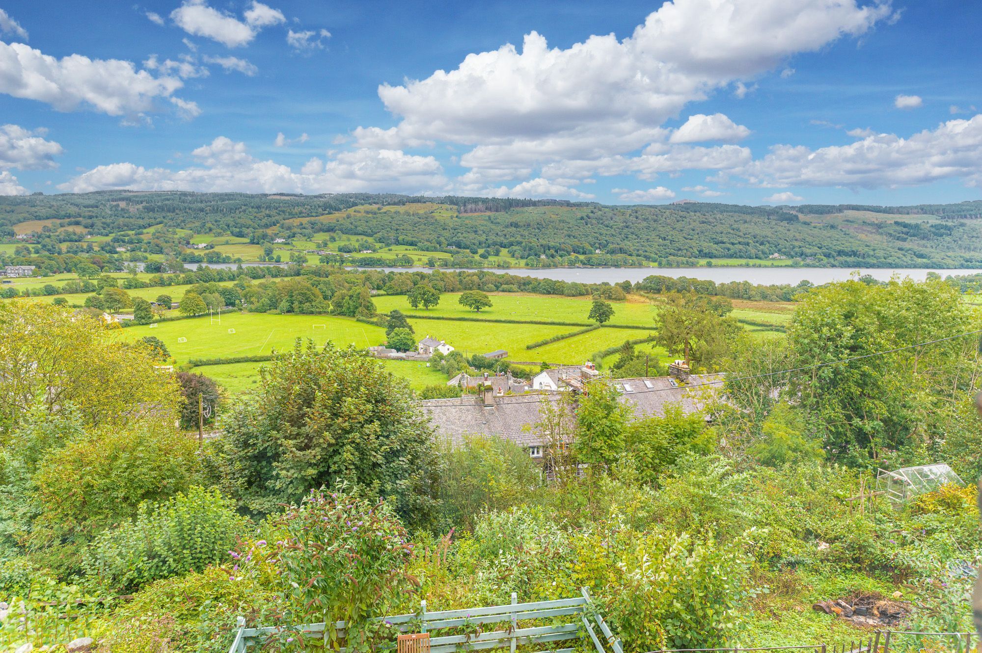 Een landelijk landschap met velden, een meer en verspreide huizen.
