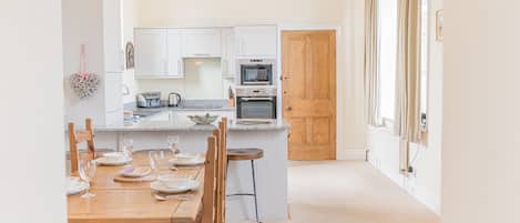 A modern kitchen with white cabinets, a wooden door, and a dining area with a wooden table and chairs.