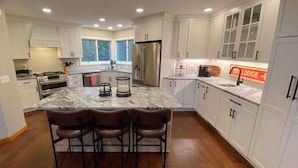 A modern kitchen with white cabinets, a marble island with bar stools, a refrigerator, and a sign reading "SKI LODGE". - C12 Homey Bretton Woods slopeside townhome. Pool/gym passes! (Bretton Woods)