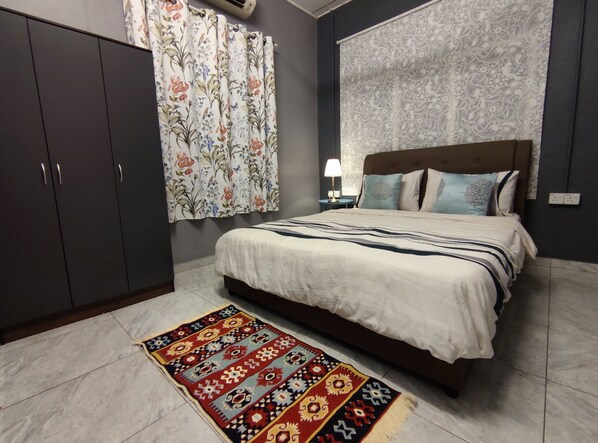 Un dormitorio con cama, mesita de noche, lámpara y una alfombra estampada.