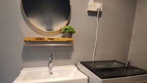 Une petite cuisine équipée avec un évier blanc, un petit miroir, une plante en pot et un réfrigérateur compact.