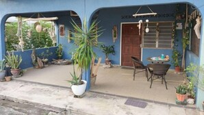 Un bâtiment bleu doté d’un patio couvert, de plantes en pot et d’une porte en bois.