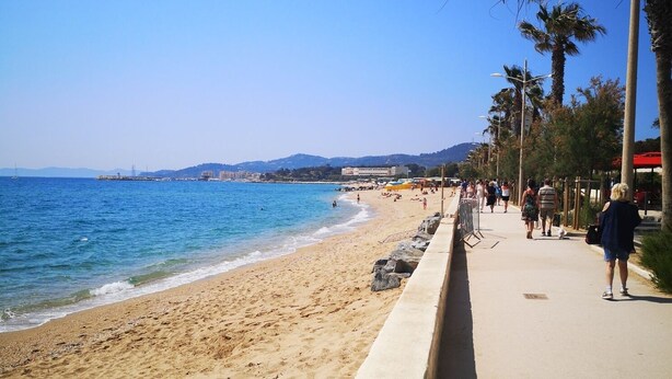Una platja amb passeig de formigó, palmeres i un cel blau clar.