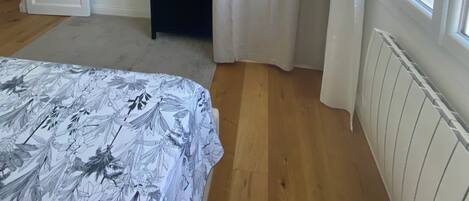 Een slaapkamer met een bed, een kledingkast, een radiator, een raam met gordijnen en een deur.