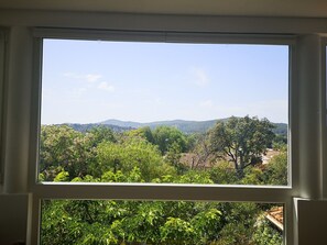 Une fenêtre donnant sur un paysage verdoyant, avec des arbres et des collines à l’horizon.