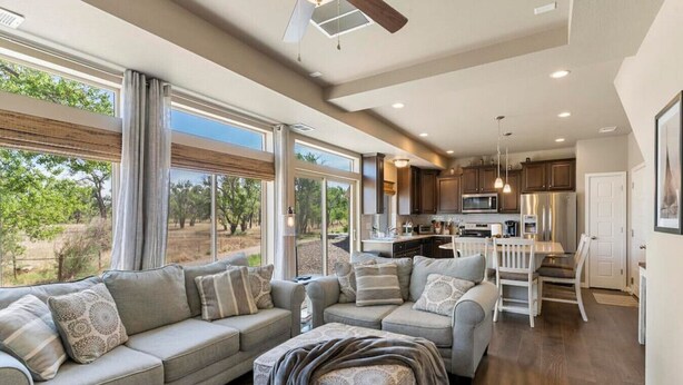 A spacious living room with a large gray sofa, a dining area with white chairs, and a kitchen with dark cabinets and stainless steel appliances. - Stylish 3 Bedroom Home with Rooftop Deck (Fountain)