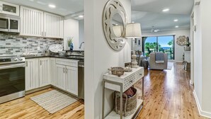 A modern kitchen with white cabinets, a microwave, and a stove. There is a dining area with a gray sofa and a large mirror on the wall.