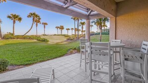 A covered patio with white chairs and a view of a golf course.