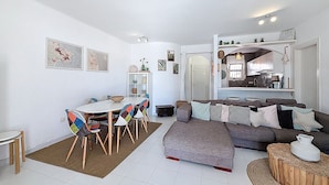 Un salon moderne comprenant un coin repas, un ensemble de canapés et une cuisine visible à travers une arche.