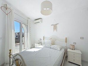 A bedroom with a bed, bedside tables, a dresser, a hanging light fixture, and a window with curtains.