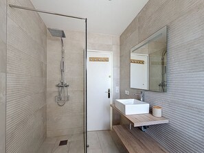 A modern bathroom with a glass shower enclosure, a white sink, and a large mirror.