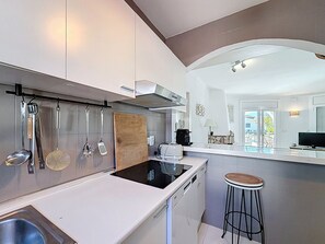 Une cuisine moderne dotée d’un îlot central, d’ustensiles suspendus et offrant une vue sur l’espace extérieur.
