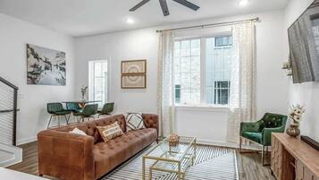 A modern living room with a brown leather sofa, green chairs, a wooden coffee table, and a ceiling fan.