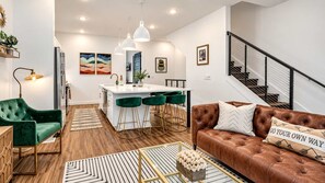 A modern living room with a brown leather sofa, green velvet armchair, and a white island with bar stools. - June’s Home • Near Broadway • Rooftop (Nashville)