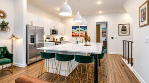 A modern kitchen with white cabinets, stainless steel appliances, a central island with bar stools, and pendant lighting. - June’s Home • Near Broadway • Rooftop (Nashville)