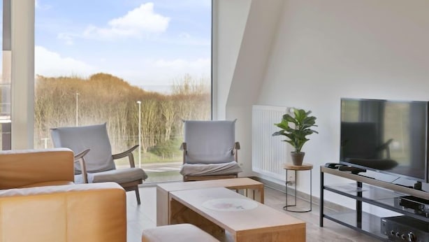 A modern living room with a large window, a flat-screen TV, and a potted plant. - L'Espérance sur mer by Interhome (Bredene)