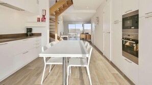 A modern kitchen with white cabinets, a wooden staircase, and a dining area with a white table and chairs. - L'Espérance sur mer by Interhome (Bredene)
