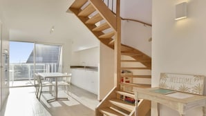A modern apartment with a wooden staircase, a balcony with a table and chairs, and a kitchen area. - L'Espérance sur mer by Interhome (Bredene)