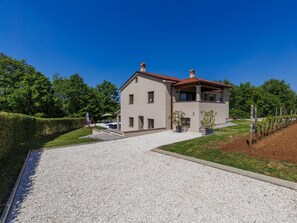 Een huis met twee verdiepingen, een grindpad, een terras en een wijngaard op de achtergrond.