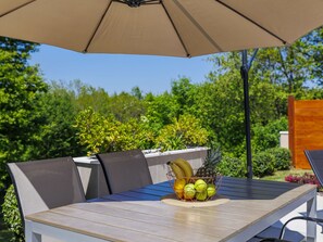 A table with a woven placemat, a fruit basket, and a large umbrella. - Apartment Eroa by Interhome (Rovinj/Žminj)