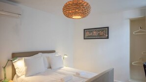 Una cama bien hecha con sábanas y almohadas blancas, una lámpara colgante y un cuadro en la pared.