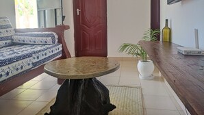 Un soggiorno con un divano, un tavolino rotondo, una pianta in vaso, una bottiglia di vino e una TV a schermo piatto montata a parete.