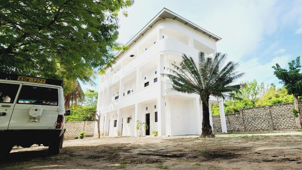 Un edificio bianco a più piani con un cortile centrale, circondato da alberi e un muro in pietra.