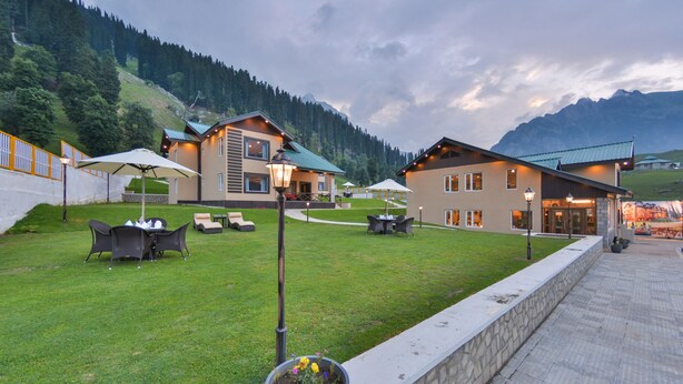 A hotel with outdoor seating, a well-maintained lawn, and mountain views. - Pine Spring Resort Sonamarg (Gund)