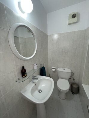 Ein Badezimmer mit Waschbecken, Spiegel, zwei Toiletten und einem Mülleimer.