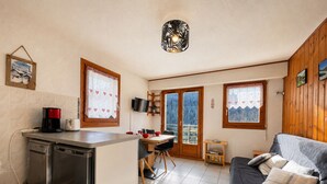A compact kitchen with a dishwasher, a dining area with a table and chairs, a sofa, and a wooden ceiling.