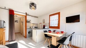 A compact living space with a kitchenette, a dining area, a TV mounted on the wall, and a sofa.