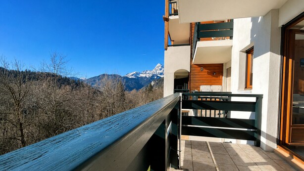A balcony with a view of mountains, a wooden railing, and a tiled floor.