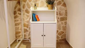 A white cabinet with two doors, a shelf with books, a potted plant, and a wall with a stone pattern.