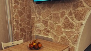 A room with a stone wall, a flat-screen TV displaying 'NONNA VITTORIA APARTMENTS', a wooden table with a fruit bowl, and a white chair. - Nonna Vittoria Apartments, Renovated apartments in Puglia (Mola di Bari)