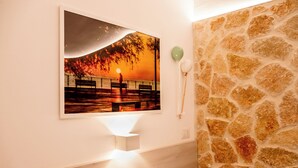 A room with a stone wall, a mounted picture of a sunset, and a white bedside table. - Nonna Vittoria Apartments, Renovated apartments in Puglia (Mola di Bari)