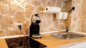 A kitchen with a stone wall, a coffee machine, a sink, and a power outlet. - Nonna Vittoria Apartments, Renovated apartments in Puglia (Mola di Bari)