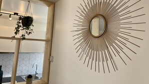 A bathroom with a sunburst mirror design, a hanging plant, and a geometric tile backsplash. - Le Cosy - Towncenter (Bayeux)