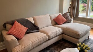 Un divano beige componibile con cuscini decorati, un tavolino e una finestra vista verde.