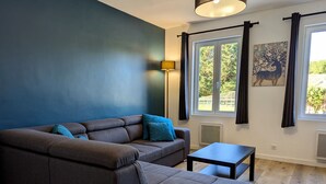 Un salon moderne avec un canapé d’angle, une petite table et une grande fenêtre agrémentée de rideaux.
