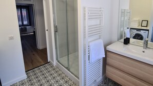 Une salle de bain moderne avec une douche en verre, une serviette blanche sur le radiateur, un lave-linge et un lavabo avec un miroir.