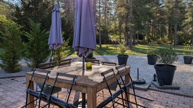 Une table en bois, avec des chaises et des parasols, dans un cadre de jardin.