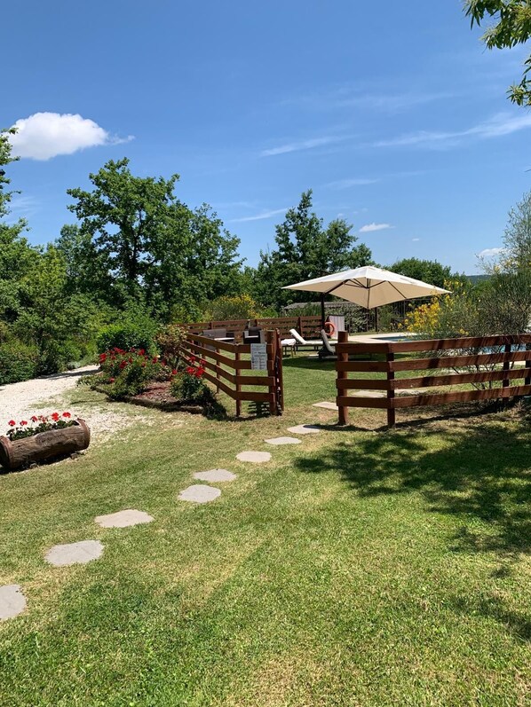A wooden fence with a bench and an umbrella, a paved path, and a grassy area with stepping stones.
